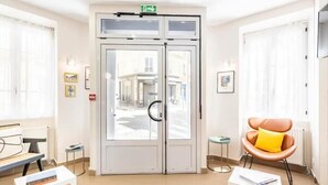A hotel lobby with a revolving door, a reception desk, a seating area with a chair, and a small table with a book. - Hotel Bonsejour Montmartre (Paris)