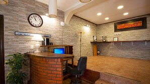 Zona de recepción con mostrador de ladrillo, una computadora, una silla, un reloj y una lámpara de pared.