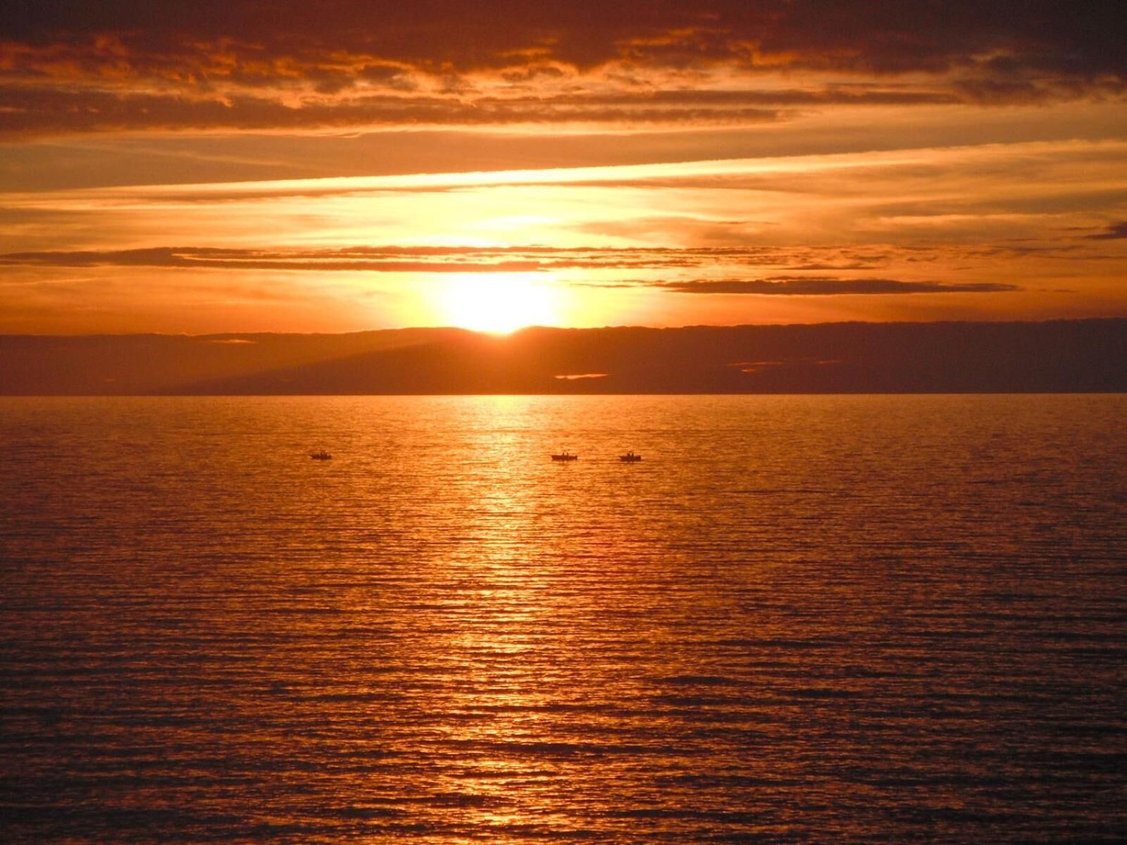 Atardecer sobre un mar tranquilo con barcos.