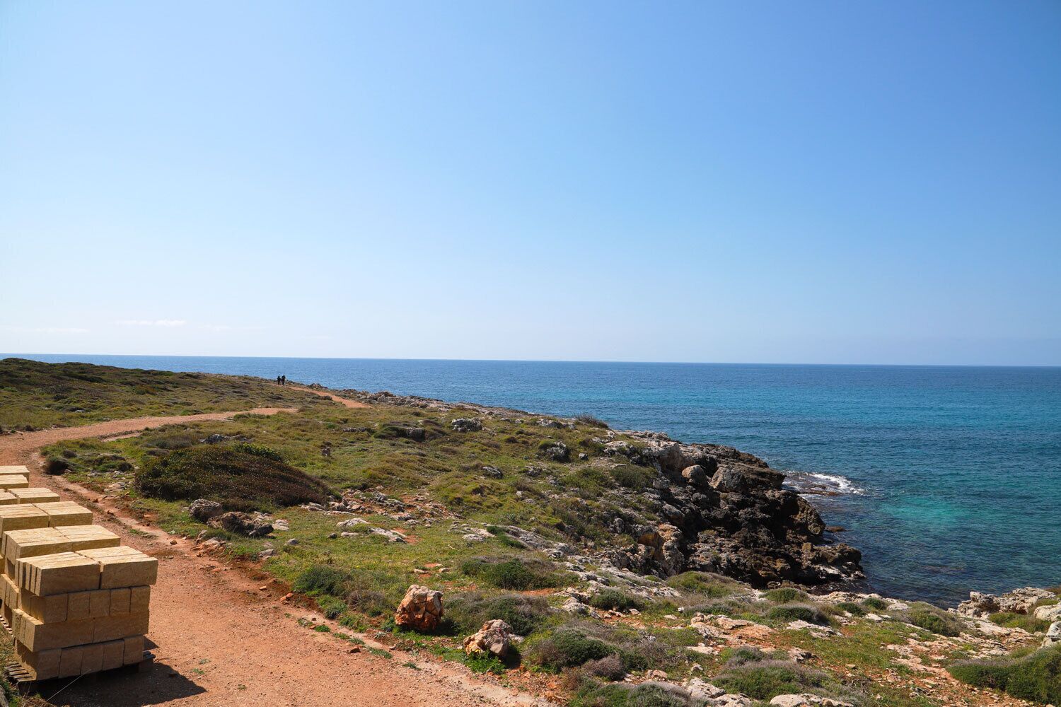 Un sentier côtier bordé d’un tas de briques et d’une plage rocheuse.