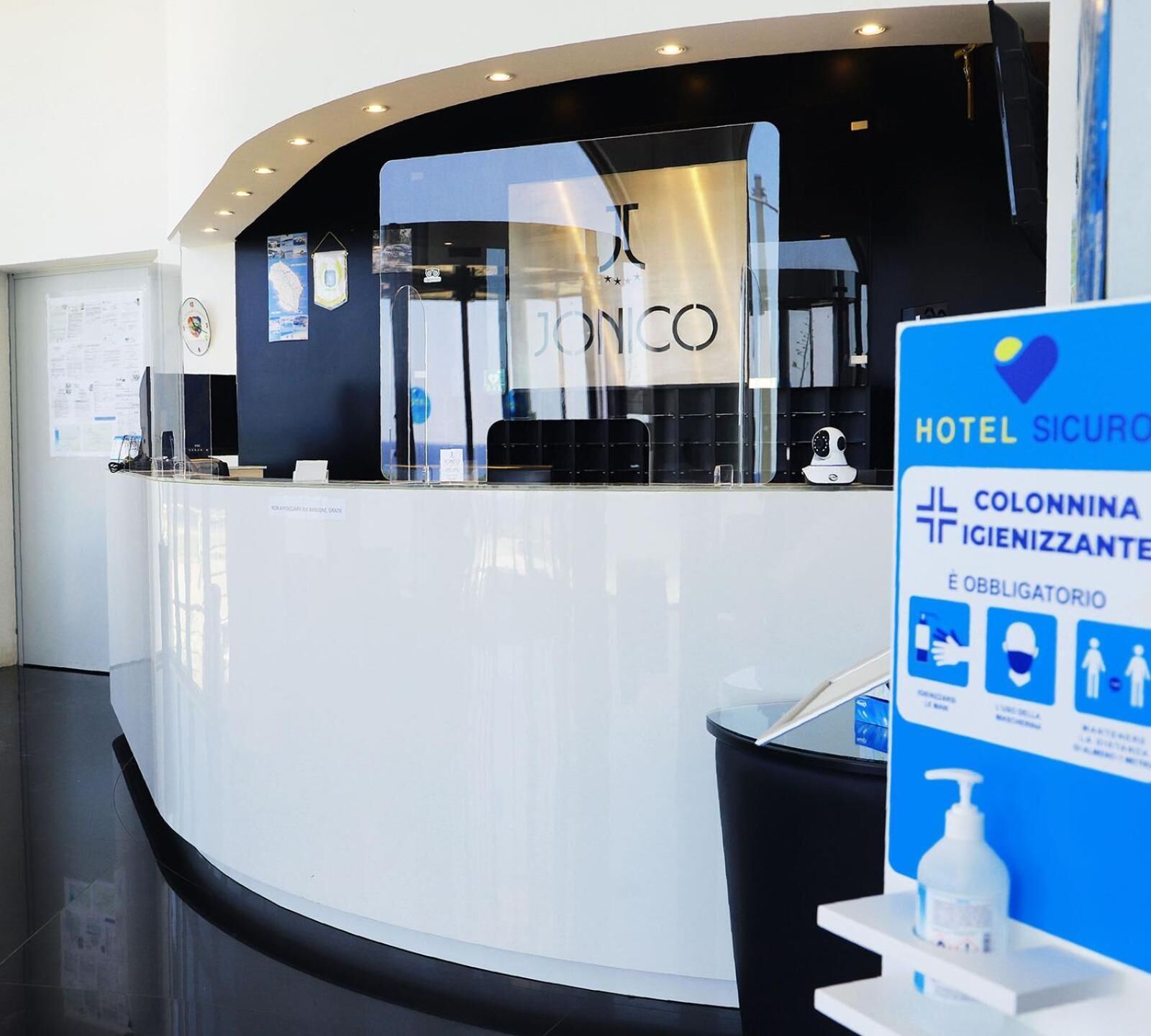 A hotel reception desk with a modern design, a visible logo, and a sign indicating hotel security and mandatory safety measures.