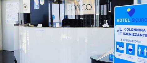 A hotel reception desk with a modern design, a visible logo, and a sign indicating hotel security and mandatory safety measures.
