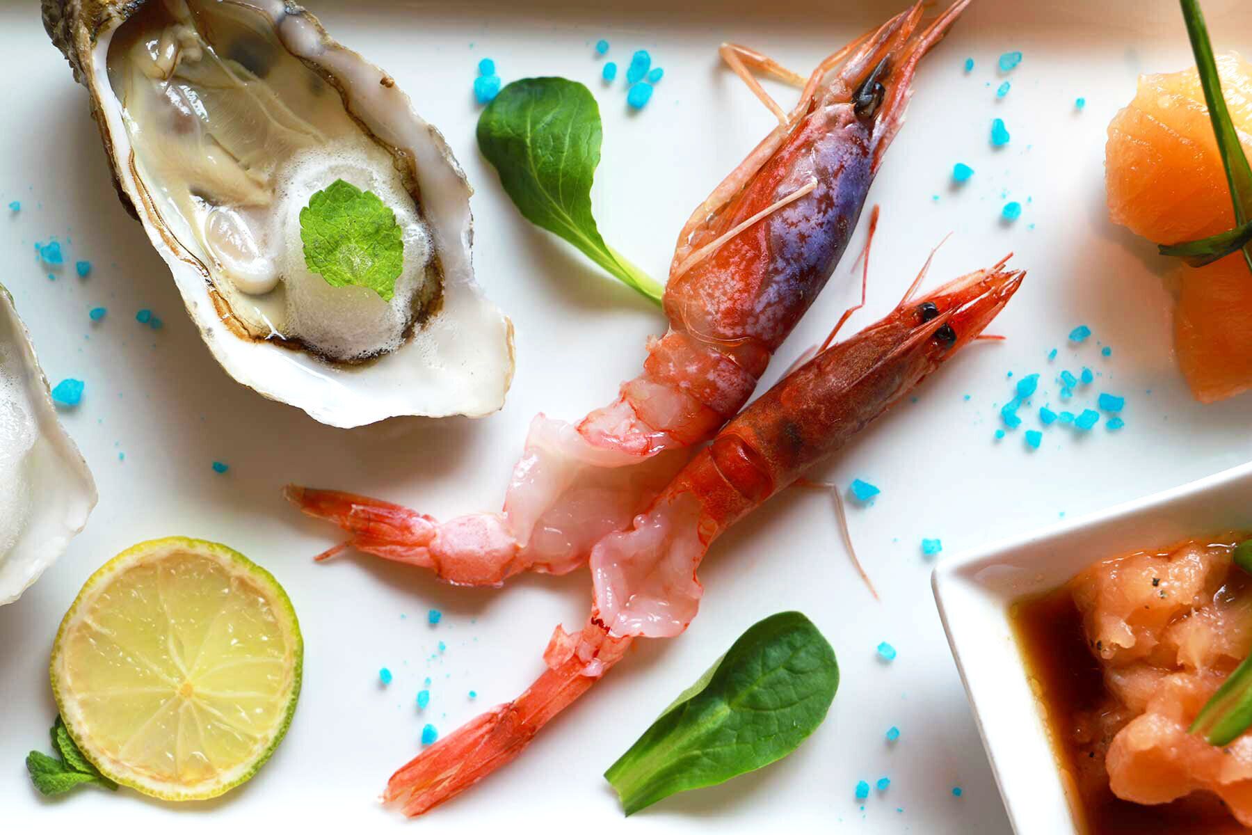 En fiskeret med rejer, en østers og en skive citron på en hvid tallerken.