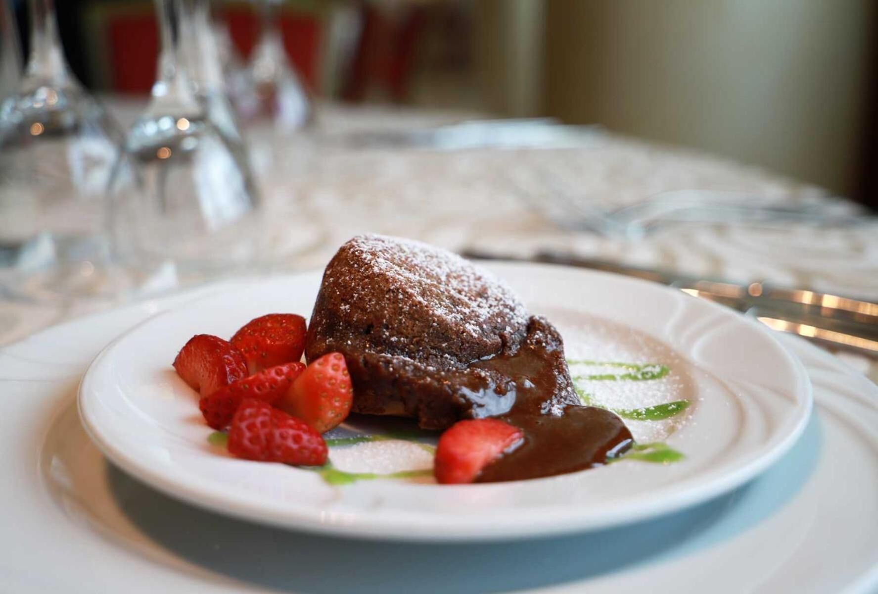A dessert plate with a chocolate lava cake, strawberries, and a chocolate sauce.