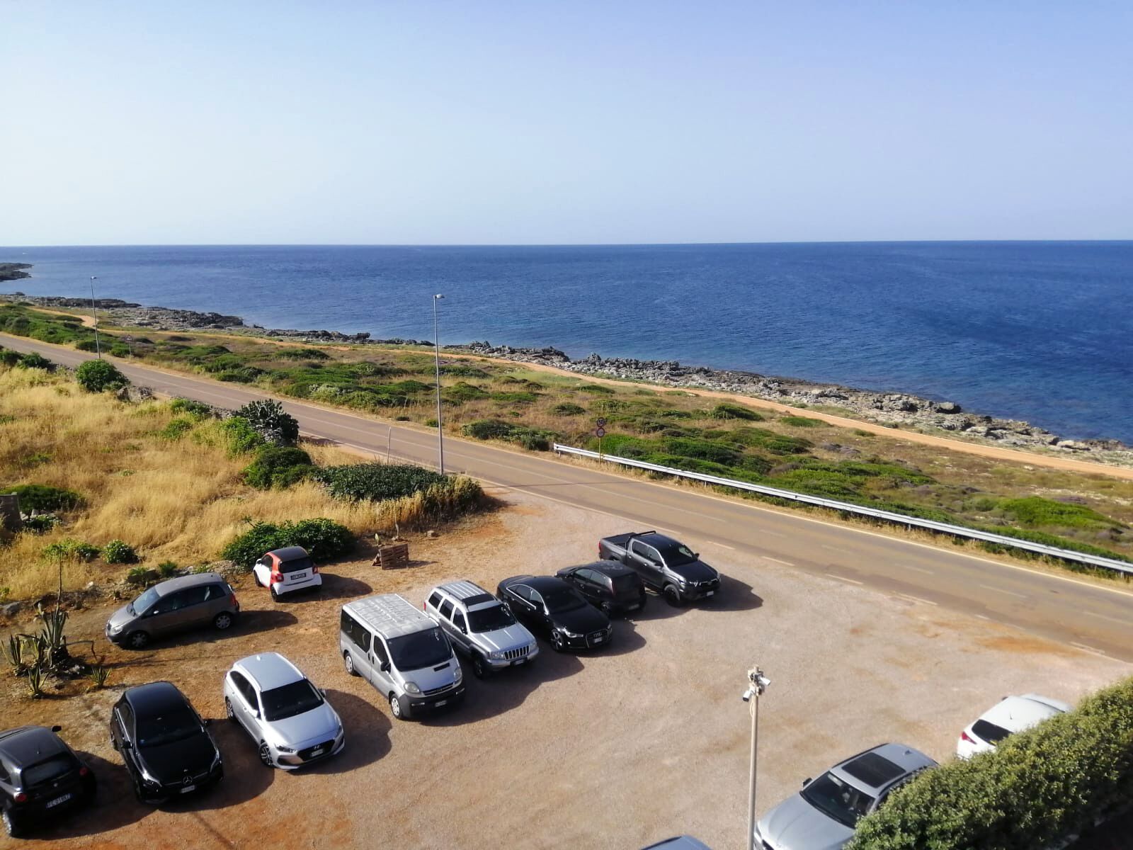 Un estacionamiento con varios autos y una carretera que lleva a una costa rocosa.