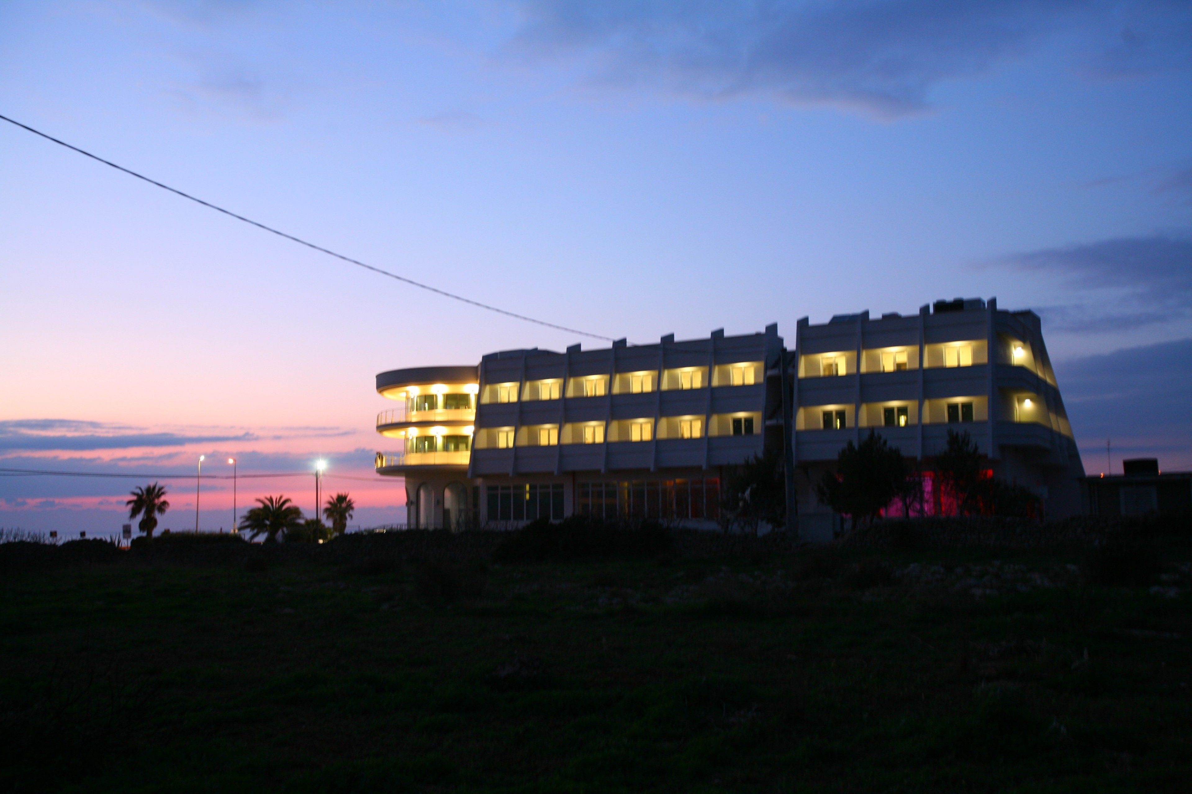 Un immeuble à plusieurs étages avec des fenêtres illuminées, probablement un hôtel, au crépuscule.