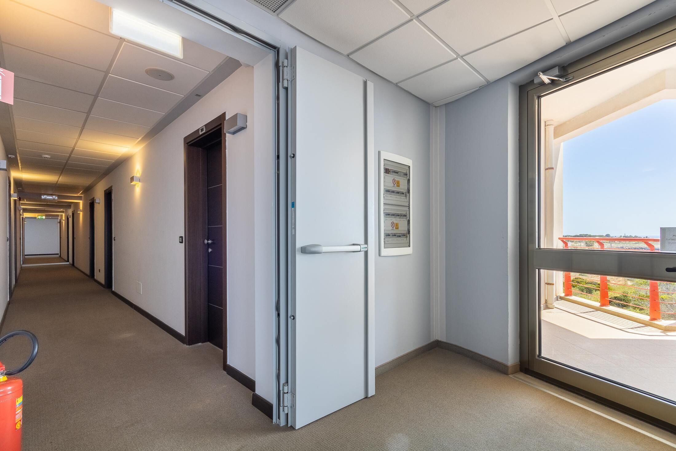 A hotel corridor with a door leading to a balcony with a view.