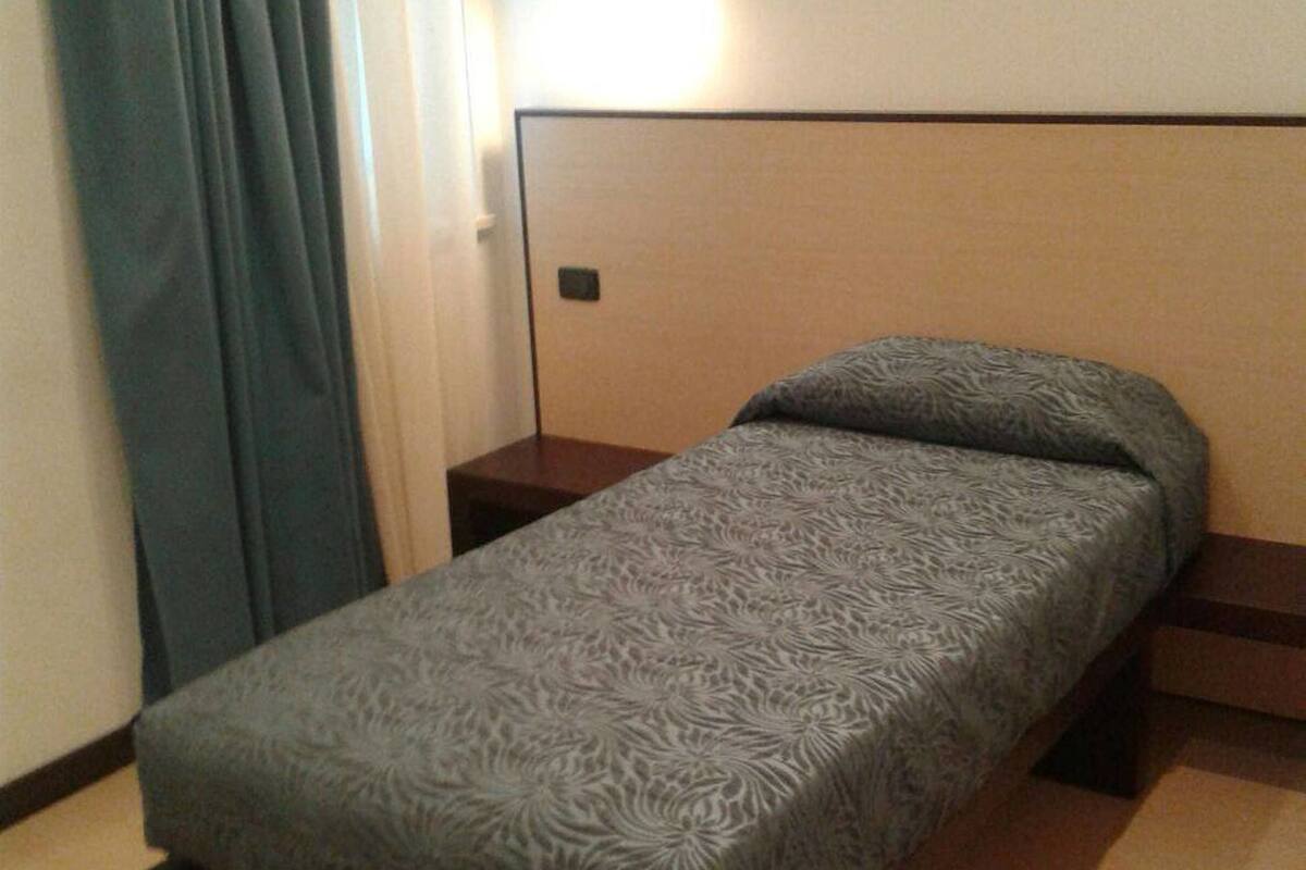 A single bed with a patterned bedspread, a bedside table, and a wall-mounted light.