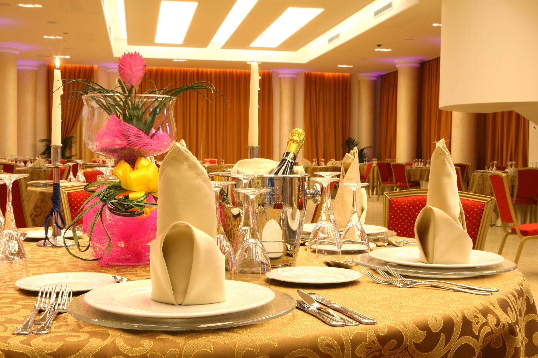 A banquet table set with plates, cutlery, and a centerpiece with flowers and a champagne bottle.