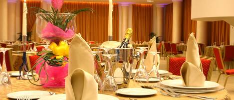 A banquet table set with plates, cutlery, and a centerpiece with flowers and a champagne bottle.
