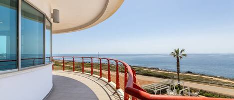 A balcony with a curved railing overlooking a beach and the ocean.