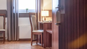 Et hotelværelse med en træstol, et lille bord med en lampe og et vindue med gardiner.