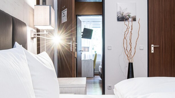 Et hotelværelse med en seng, natlampe og udsigt til gangen.
