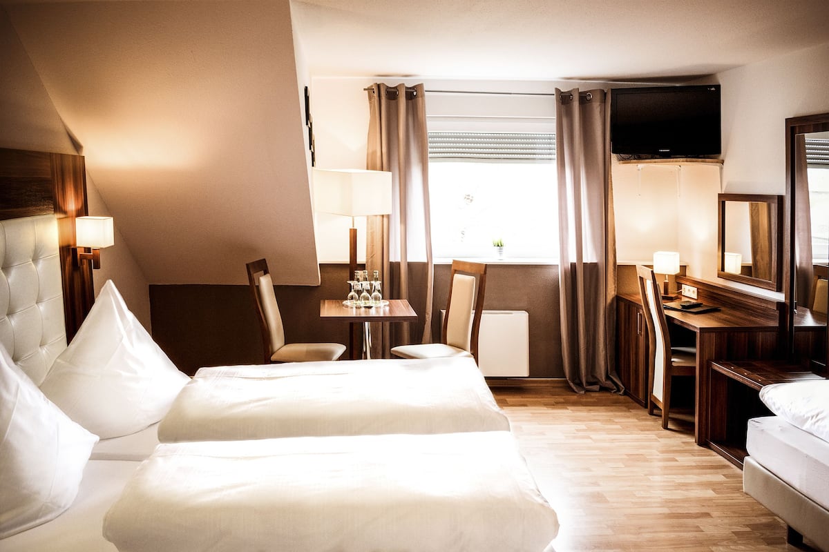 A hotel room with two beds, a desk, a chair, a TV, and a window with curtains.