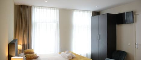 Quarto de hotel com cama, cadeira, guarda-roupa e televisão.