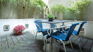 Un patio con una mesa y sillas, rodeado de plantas de bambú y una estatua.
