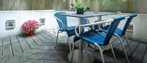 Un patio con una mesa y sillas, rodeado de plantas de bambú y una estatua.