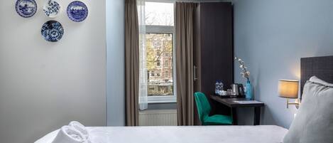 Habitación de hotel con una cama bien hecha, un escritorio con lámpara, una silla y una ventana con cortinas.