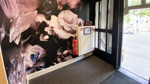 Un área de recepción con un gran mural floral, un extintor y una ventana con vista a la calle.