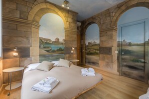 Quarto com uma cama grande, duas mesas de cabeceira e um mural de paisagem.