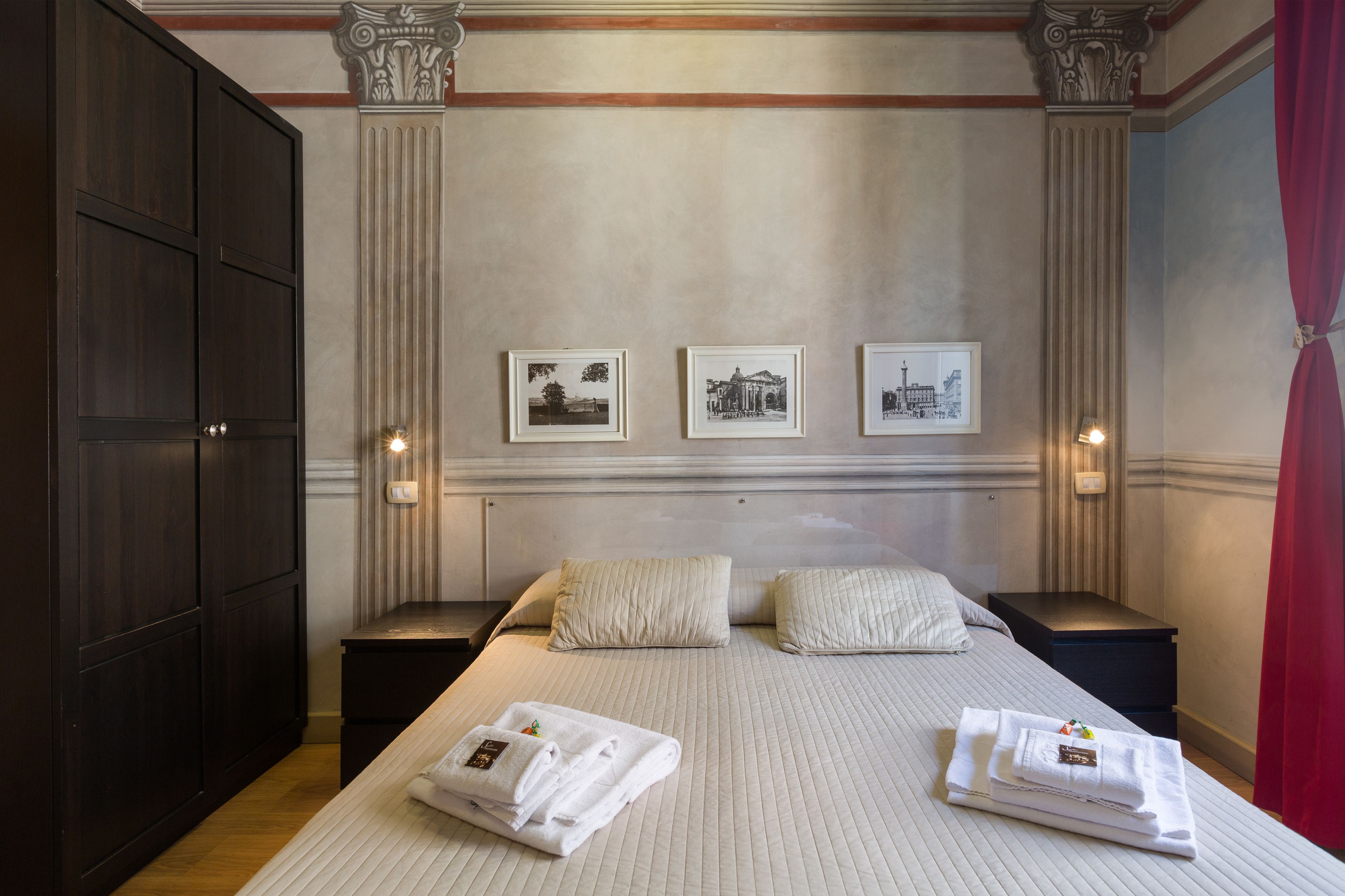 A hotel room with a large bed, two nightstands, a wardrobe, and three framed pictures on the wall.