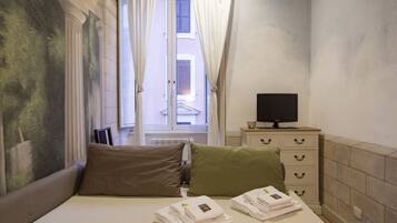 A hotel room with a bed, pillows, a TV on a dresser, and a window with curtains.