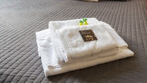 A neatly folded white towel with a tag on a bed with a grey quilted cover. - Suites Trastevere (Rome)