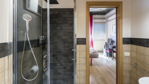 A modern bathroom with a glass-enclosed shower, a wooden-framed doorway leading to a living area, and a tiled floor. - Suites Trastevere (Rome)