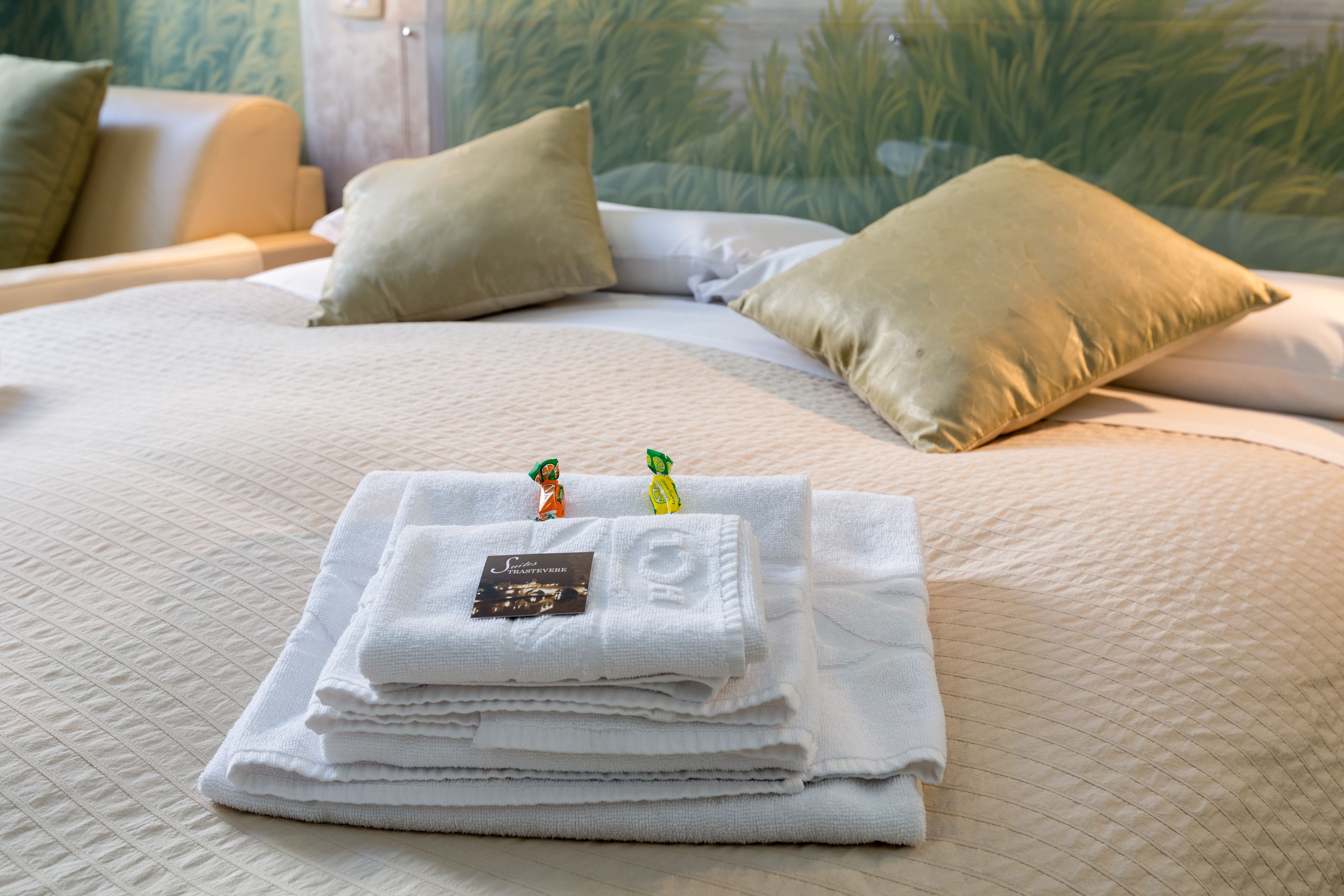 A neatly made bed with folded white towels and a small card, a beige pillow, and a view of greenery through a window.