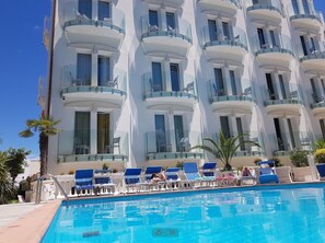 A hotel with a swimming pool, multiple balconies, and sun loungers. - Hotel Ambassador (Rimini)