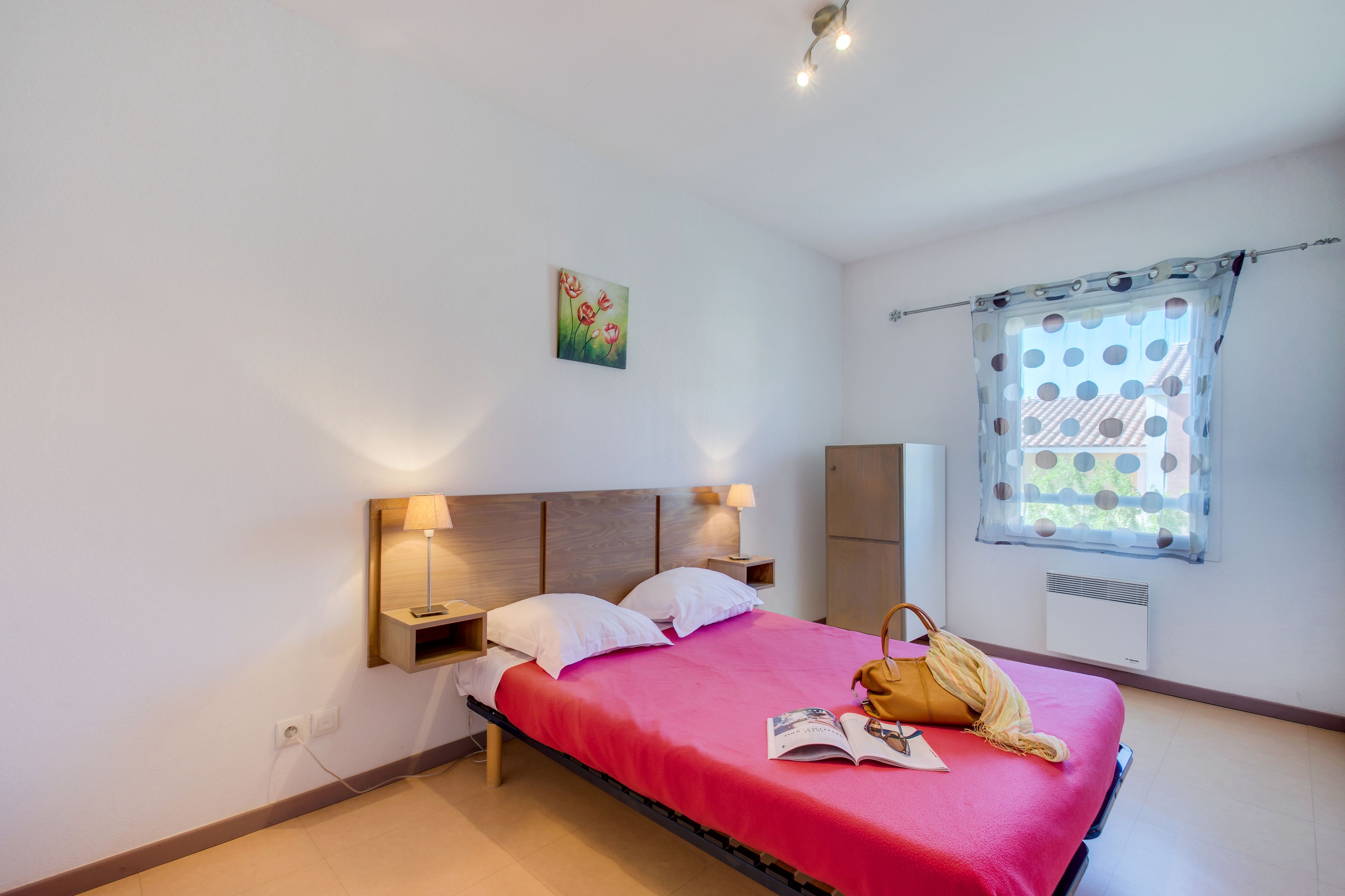 A bedroom with a bed, bedside lamps, a window with a curtain, and a painting on the wall.