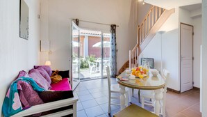 Un salon moderne comprenant un canapé, une table à manger avec des chaises, un escalier et une porte-fenêtre coulissante donnant sur un espace extérieur.