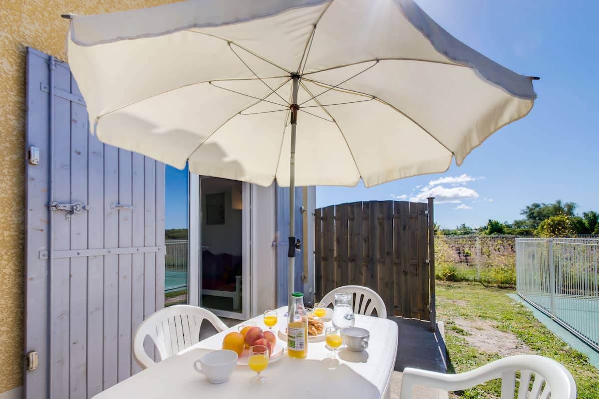 An outdoor dining area with a table set for breakfast, including fruits, beverages, and a bottle of juice.