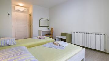 A hotel room with two beds, a chair, a desk, a mirror, and a radiator.