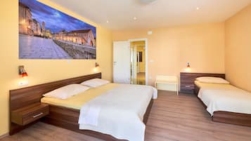 Una habitación de hotel con una cama grande, una cama más pequeña, una mesita de noche y una lámpara fijada a la pared.