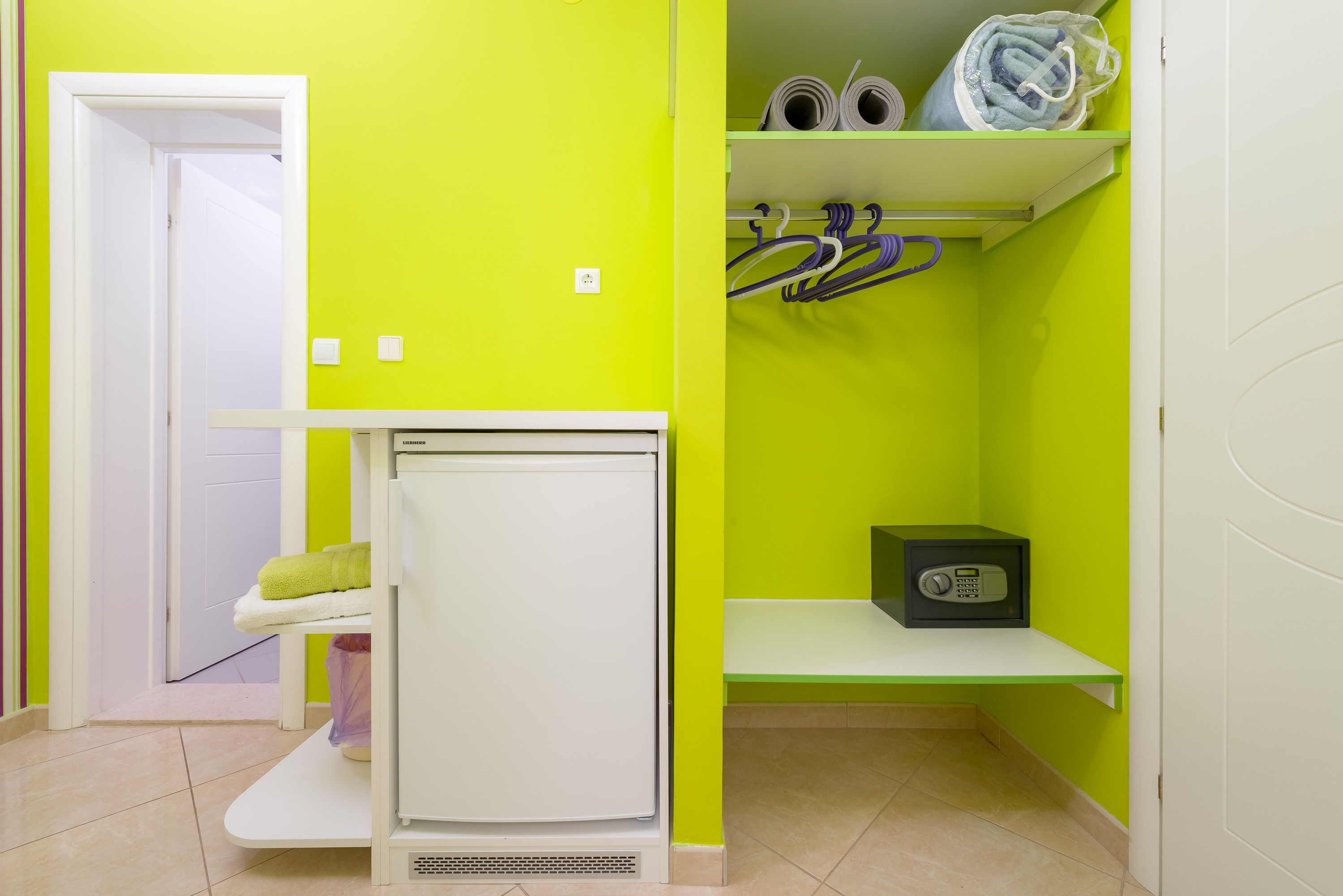 A compact room with a white refrigerator, a small shelf with a radio, and a door leading to another room.