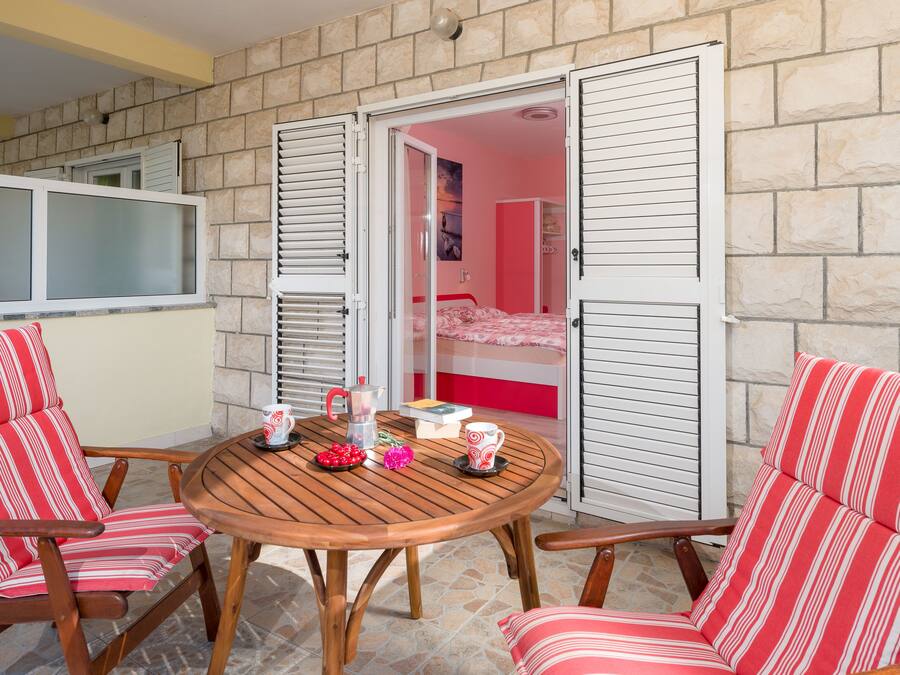 A room with a stone wall, a wooden table, two striped chairs, and a bed with pink bedding.
