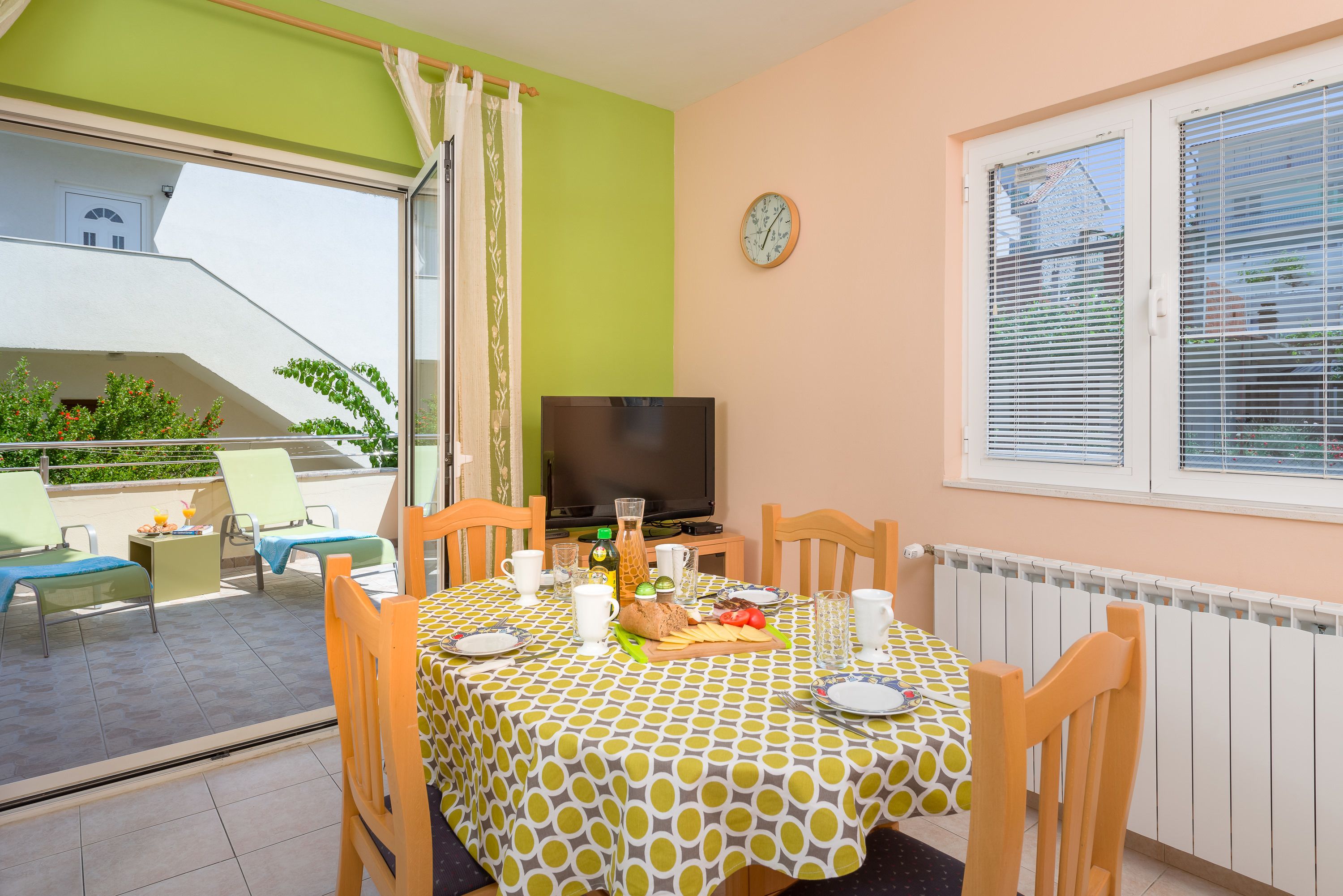Un comedor con una mesa preparada para dos personas, un televisor y vistas al balcón.