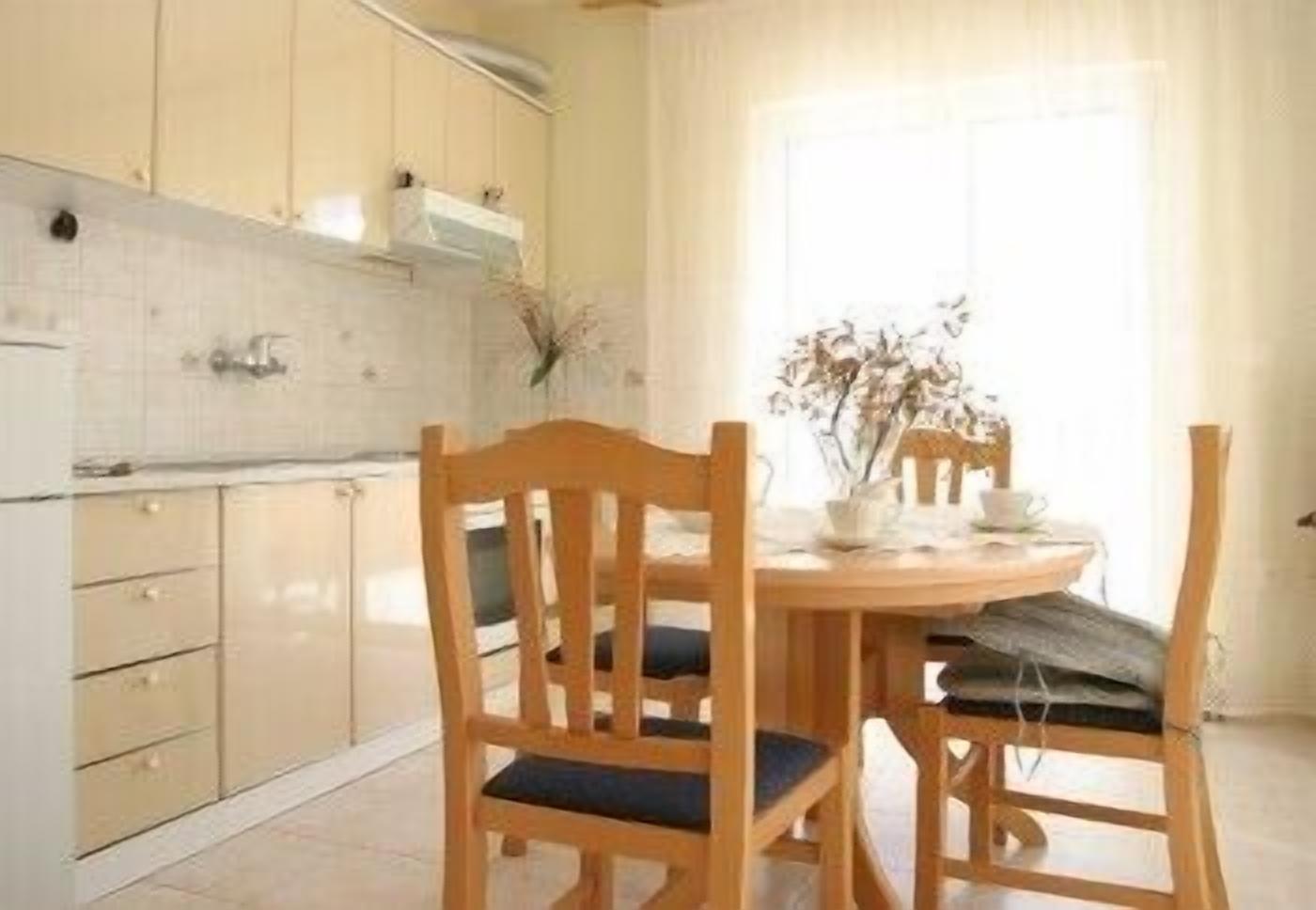 Une cuisine avec des meubles de rangement en bois, une table à manger avec des chaises et une fenêtre avec des rideaux.