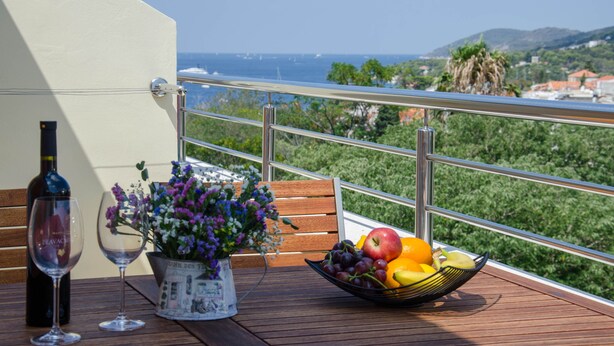 A balcony with a table set with a wine bottle, glasses, flowers, and a fruit bowl.