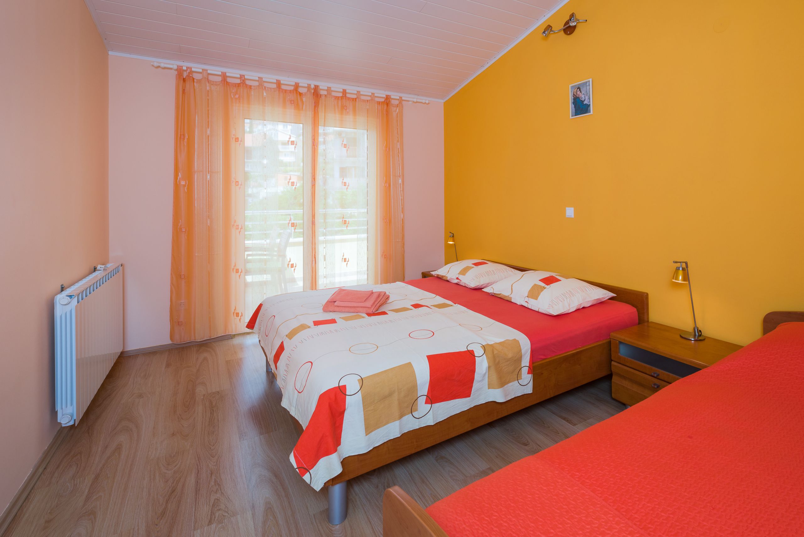 A bedroom with a bed, a bedside table, a lamp, and a window with curtains.