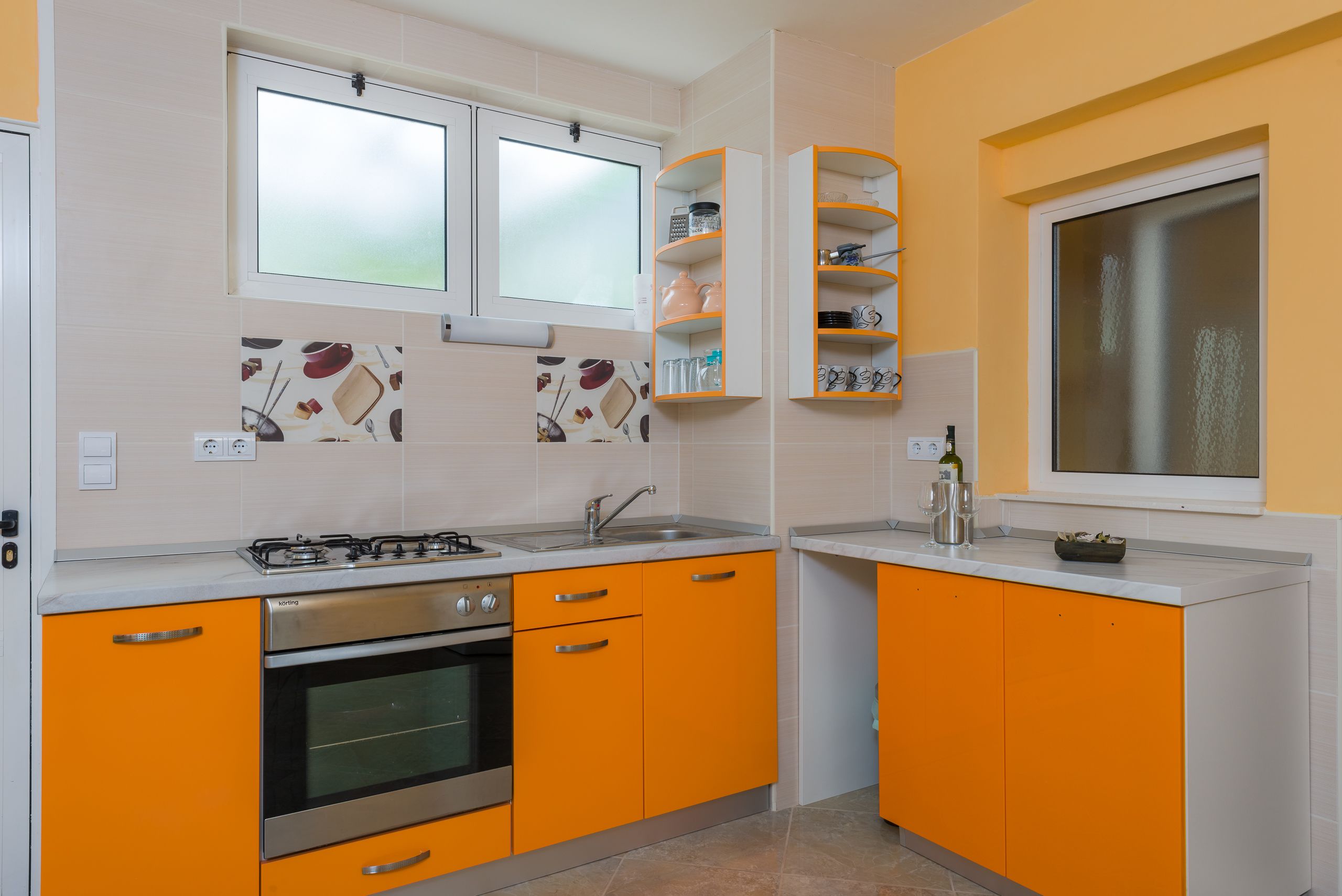 Eine Küche mit orangefarbenen Schränken, einem Gasherd und einem Fenster mit satiniertem Glas.