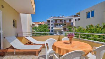 A balcony with a table and chairs, a sun lounger, and a view of neighboring buildings.