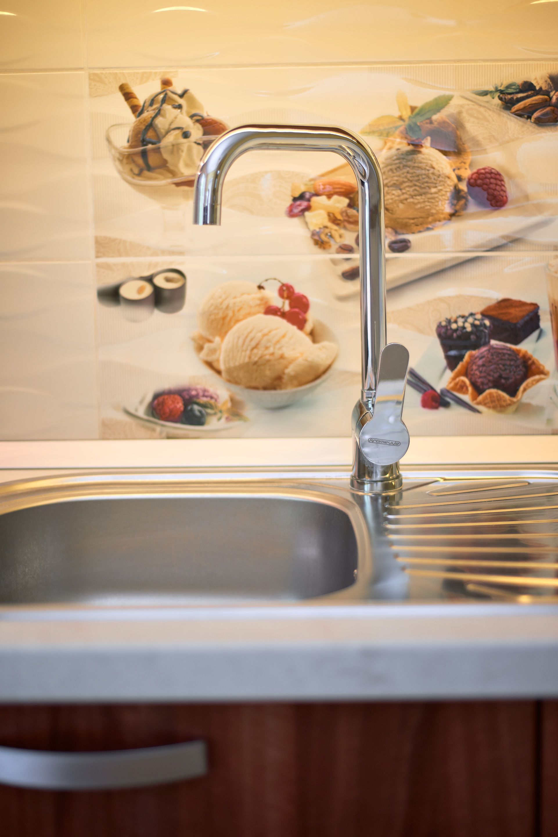 A kitchen sink with a faucet and a tiled backsplash displaying various food items.