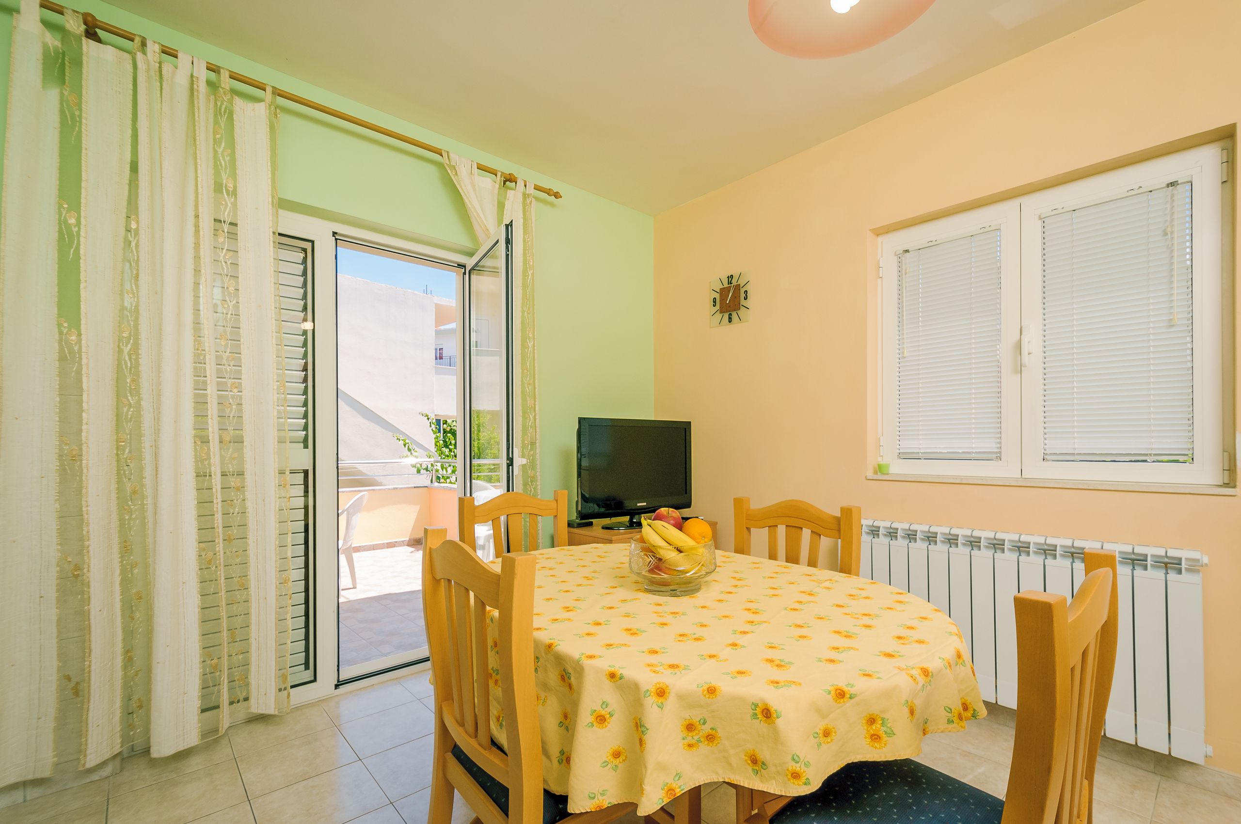 Un comedor con una mesa lista para dos, un televisor y una ventana con persianas.