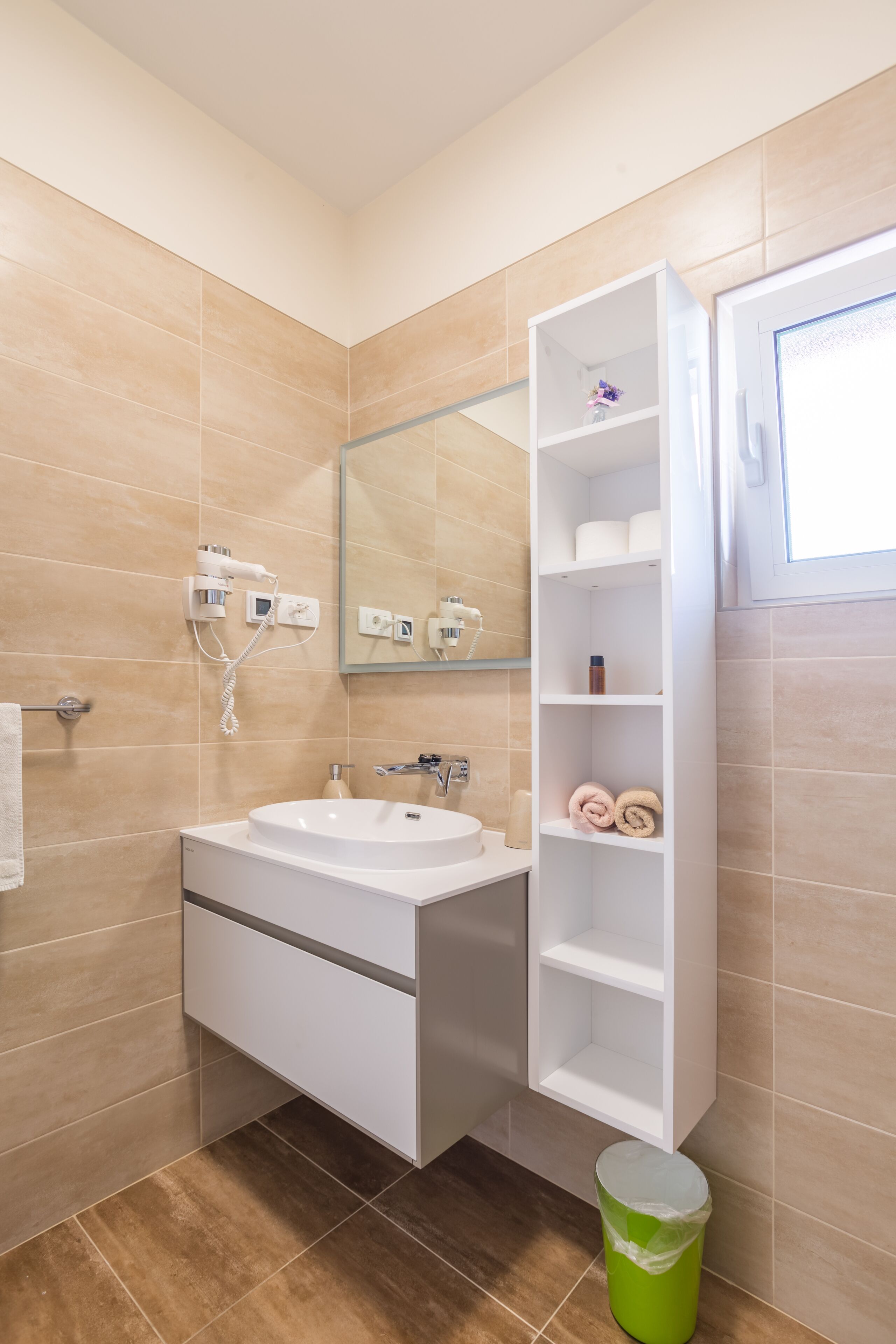 A modern bathroom with a white sink, mirror, and built-in shelves.
