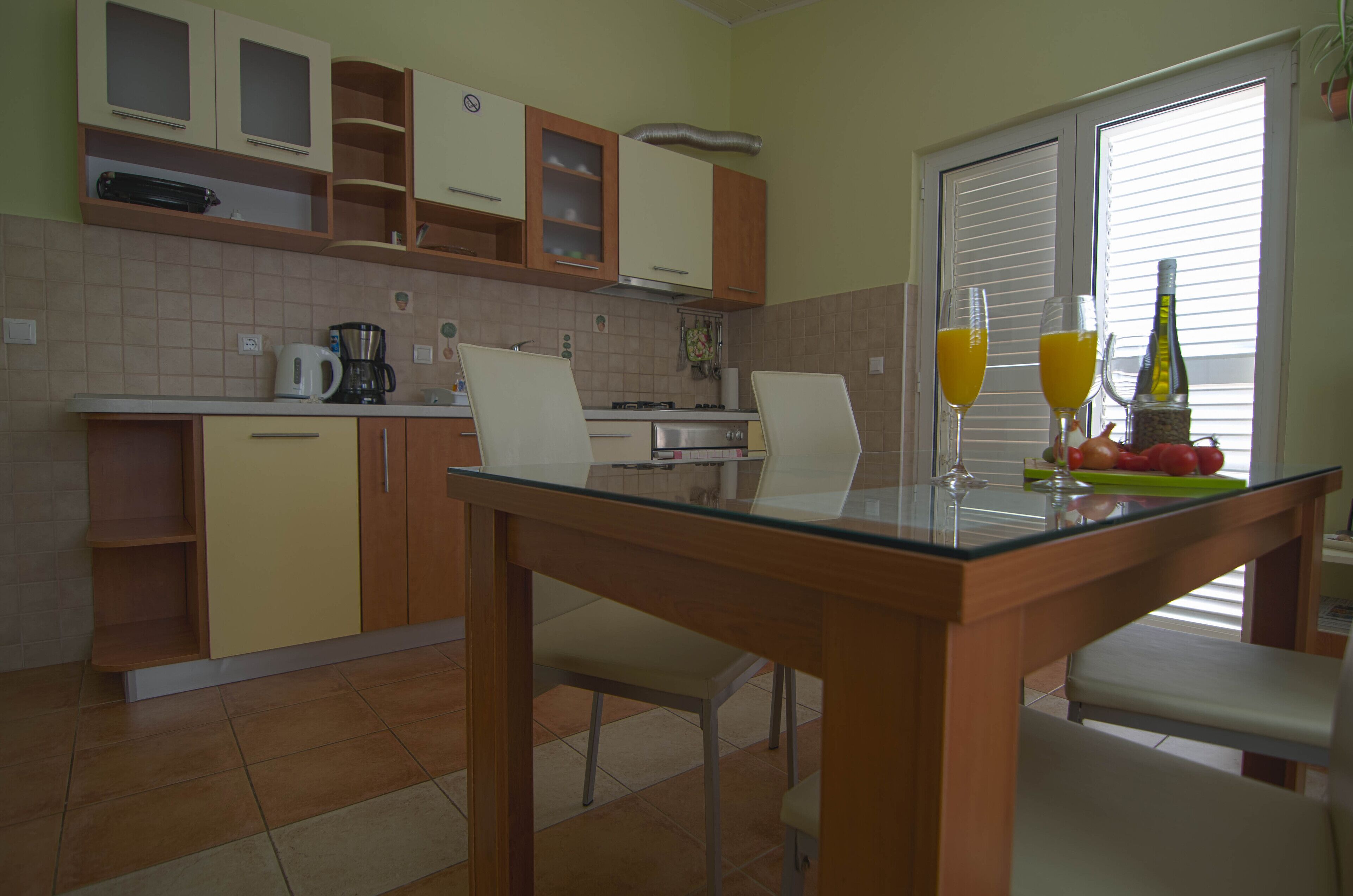 Une cuisine avec une table à manger, des chaises, une machine à café et deux verres de jus d’orange.