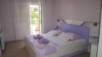 Un dormitorio con cama, mesita de noche, ventana con cortinas y vistas a un balcón.