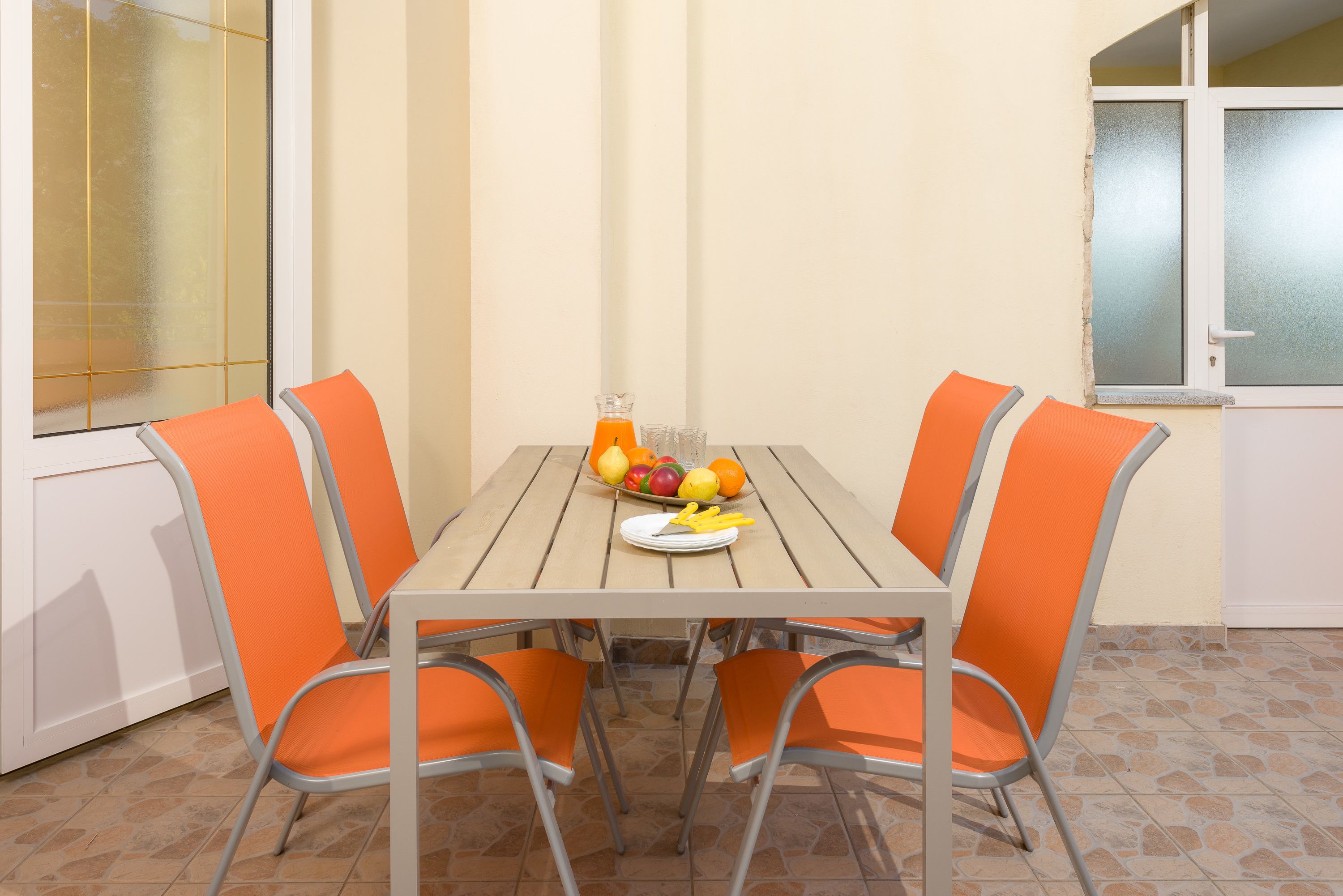 A dining table with four orange chairs, a fruit bowl, and a glass of orange juice.