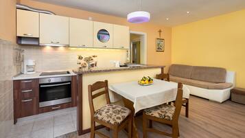 A compact kitchen with modern appliances, a dining area with two chairs, and a sofa in a yellow-walled living space.
